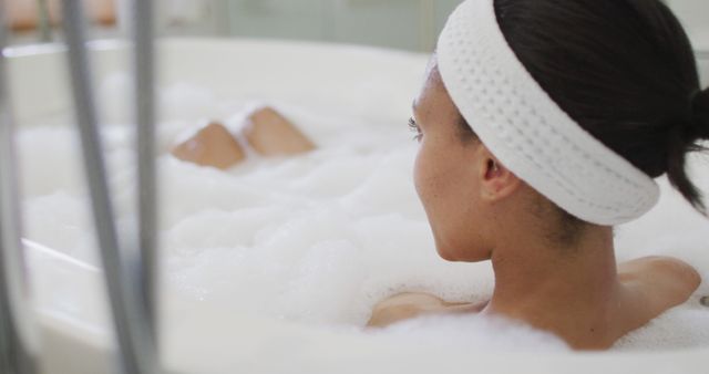 A woman with headband is relaxing in a bubble bath, enjoying a peaceful and rejuvenating moment. Ideal for promotions related to self-care, wellness, spa treatments, relaxation routines, and personal wellness blogs.
