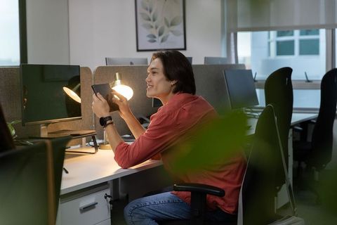 Young asian man using tablet at lit desk in modern office cubicle, casual work routine