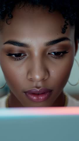 Vertical video: Woman reading on laptop under soft glow, shifting gaze and speaking