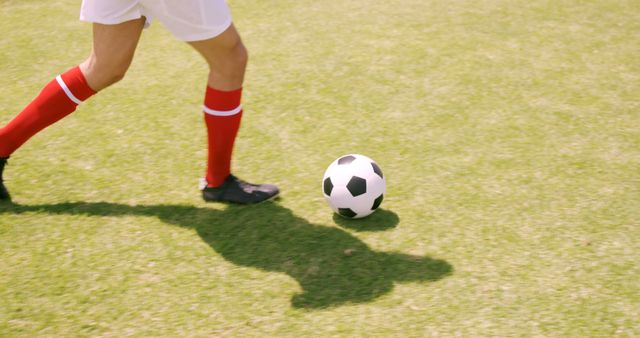 Man kicking soccer ball on a grassy field, wearing red socks. Suitable for sports and fitness promotions, articles on soccer techniques, and athletic product advertisements.