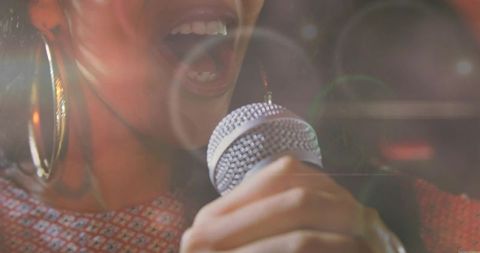 Female singer performing with handheld microphone closeup, live music lens flare