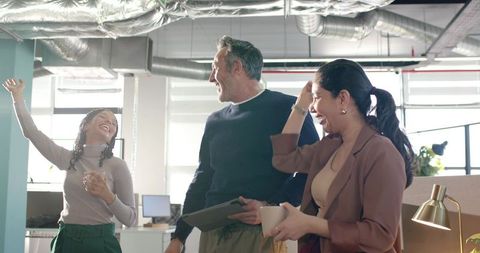 Team laughing and celebrating success in bright modern open-plan office with coffee