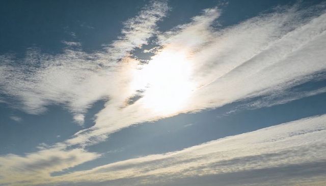 Sunlight Breaking Through Wispy Cloud Bands Creating Halo Glare Over Blue Sky