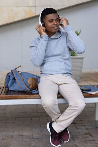 African american teen listening to music on campus bench adjusting headphones