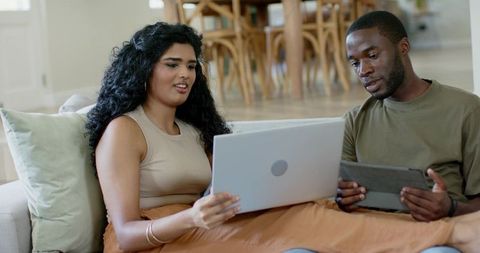 Couple collaborating on finances, reviewing animated charts on laptop and tablet in modern living ro