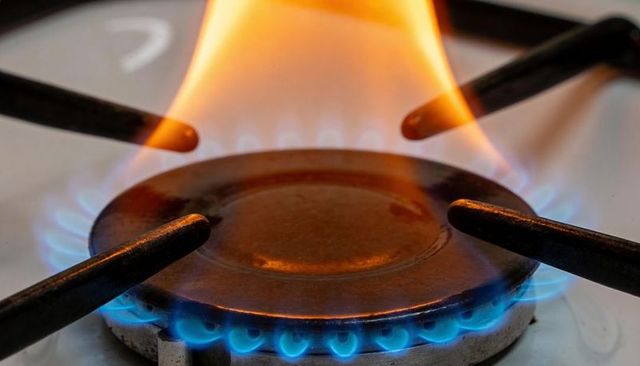 Gas burner producing blue flame ring and orange plume on cast-iron stove
