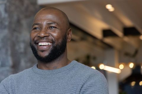 Confident african american man smiling in modern coworking lounge wearing gray knit sweater