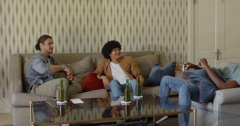 Friends sitting and chatting on beige sectional with glass coffee table and green bottles