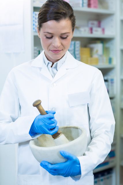 Pharmacist grinding medicine in mortar and pestle, wearing blue gloves and white coat, in a pharmacy. Ideal for illustrating pharmaceutical processes, healthcare professions, drug preparation, and medical environments.