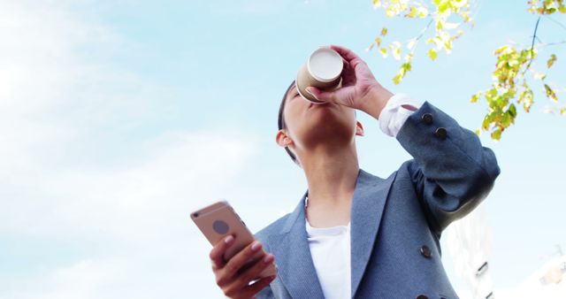 Business professional sipping coffee while using smartphone outside, wearing suit and enjoying fresh air. Perfect for business, mobile technology, urban work life concepts. Ideal for corporate presentations, business websites, and lifestyle blogs.