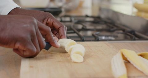 African american man slicing banana on wooden cutting board in home kitchen closeup