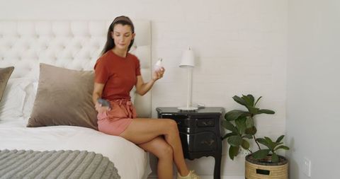 Woman Preparing for Day in Minimalist Bedroom, Holding Spray Bottle