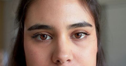 Closeup headshot of adult woman gazing, brown eyes and natural skin texture in soft light