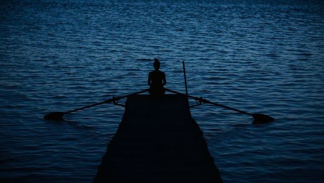 Solitary woman sitting on dock with oars at twilight over calm lake serene silhouette