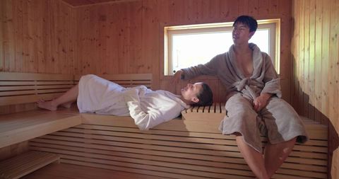 Asian and african american couple relaxing in wooden sauna wearing bathrobes spa retreat
