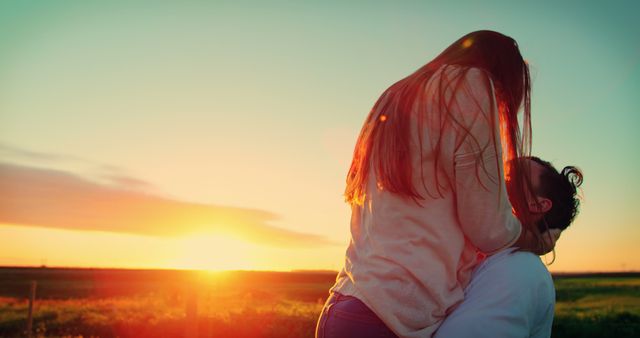 A young Caucasian couple enjoys a romantic moment at sunset in an open field, with copy space. Their affectionate embrace captures a sense of love and connection against the vibrant backdrop of the setting sun.