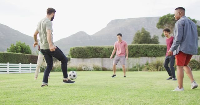 Group of diverse friends enjoys playing soccer on a lush grass field with scenic mountains in the background. Ideal for promoting outdoor activities, team sports, friendship, community events, wellness, and fitness campaigns.