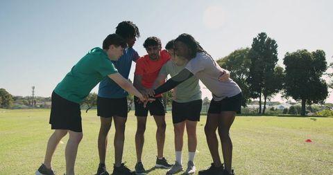 Diverse male teammates huddling and performing high-knee hop drill on grassy outdoor field