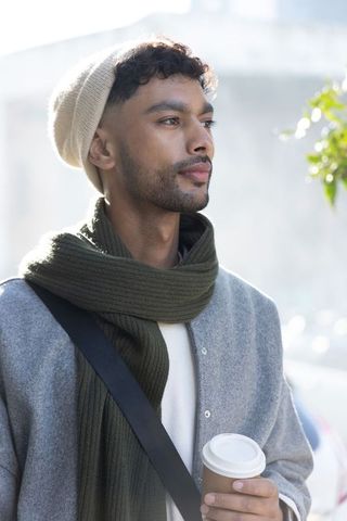 Asian man holding coffee cup, gazing right, wearing beanie and scarf, urban winter portrait