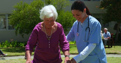 Nurse assisting elderly woman with walker in nursing home garden