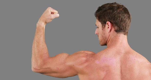 A muscular Caucasian man flexes his bicep to showcase his physical fitness, with copy space. His well-defined muscles reflect dedication to strength training and bodybuilding.