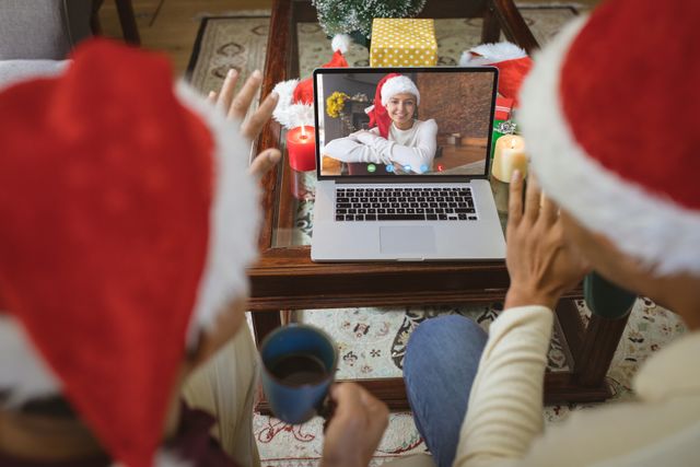 Couple wears Santa hats, enjoying video call with happy woman on laptop at home. Cozy holiday ambiance with candles, presents visible. Perfect for holiday communication themes, virtual celebration promotions, festive greetings.