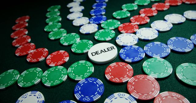 Dealer chip encircled by colorful poker chips in red, blue, and green on a gaming table. Suitable for illustrating concepts related to gambling, casino games, strategy, and gaming activities. Ideal for use in articles, blogs, advertisements, and promotional materials related to betting.