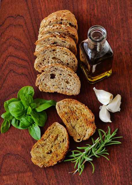 Sliced Whole Grain Bread With Olive Oil, Fresh Herbs, and Garlic Cloves on Wooden Surface - Download Free Stock Photos Pikwizard.com