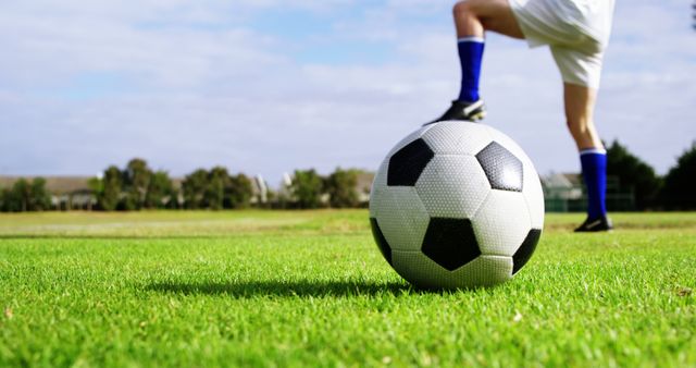 Soccer player preparing to kick ball on lush green field. Suitable for sports-related materials, fitness promotions, athletic motivation, outdoor activities advertisements, and soccer training guides.