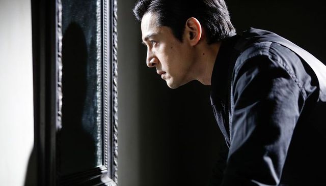 Leaning man studying ornate mirror reflection, dramatic sidelit silhouette, contemplative