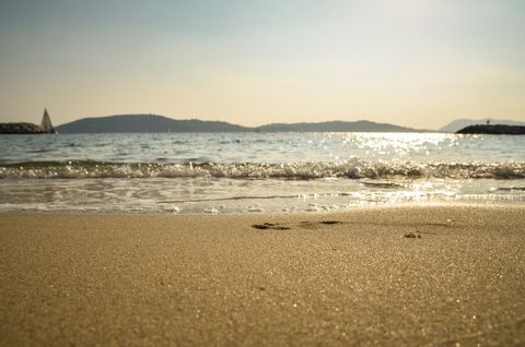 Golden Sand Beach Lapping Gentle Waves, Sunlight Glittering on Water, Distant Sailboat
