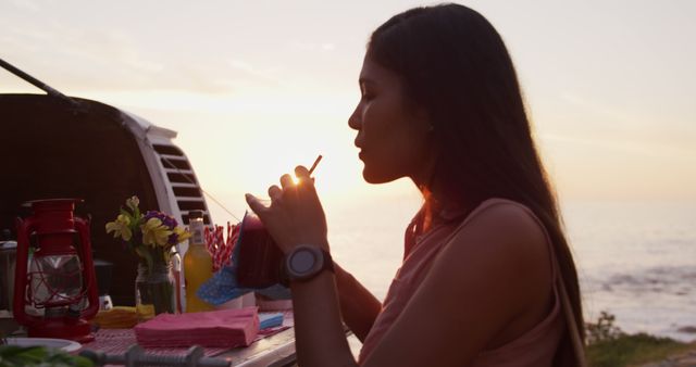 Young Woman Sipping Drink at Seaside Evening Picnic - Download Free Stock Images Pikwizard.com