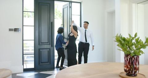 African american couple greeting friend and twirling woman in black dress in modern foyer