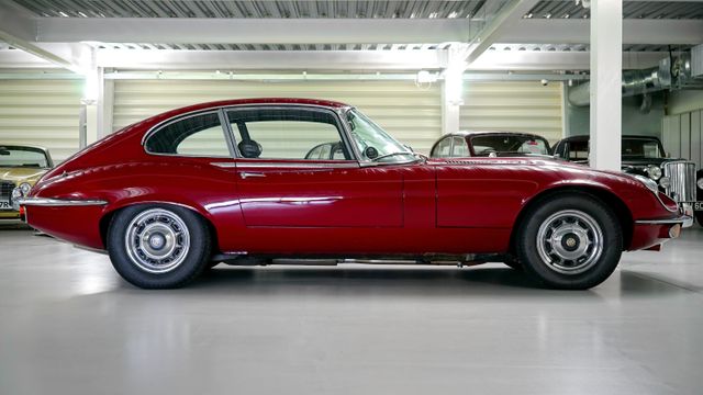 Classic red Jaguar E-Type parked in a well-lit garage with a white floor, highlighting its sleek and iconic design. The vintage feel and timeless appeal of this car make it perfect for use in automotive blogs, retro-themed content, or advertisements targeting car enthusiasts and collectors.