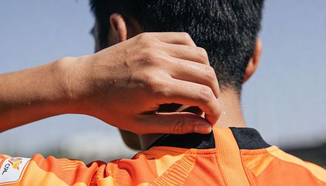 Adjusting jersey collar on male athlete neck close-up in bright orange sports jersey at stadium