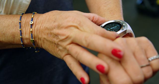 The close-up image showcases a woman with red nail polish adjusting her smartwatch. She is wearing two bracelets and a ring on her finger, indicating a blend of technology and fashion. This image can be used in advertisements related to smartwatches, jewelry, health and fitness apps, or fashion accessories.