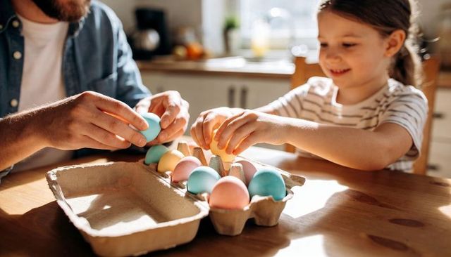 Father and daughter painting and arranging pastel easter eggs at sunlit kitchen table