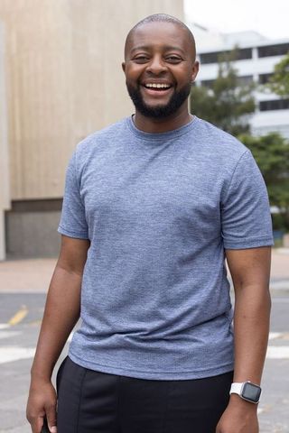 Smiling man standing in urban plaza wearing gray t-shirt and white smartwatch