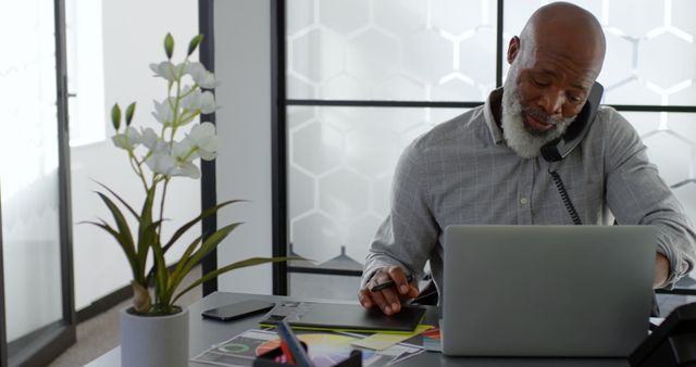 Mature Businessman Working on Laptop While Using Phone in Modern Office - Download Free Stock Images Pikwizard.com