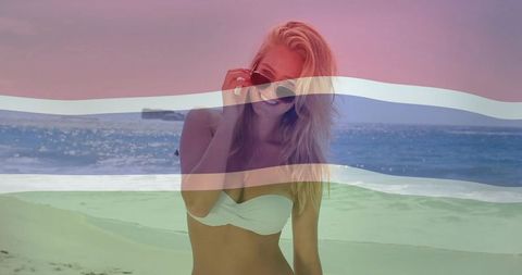 Smiling woman posing on sunny beach wearing white bandeau bikini with color bands