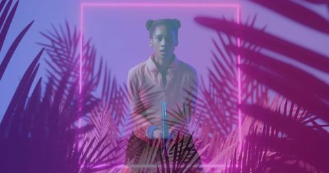 Posing young woman holding neon tube in magenta palm foliage with glowing gradient frame