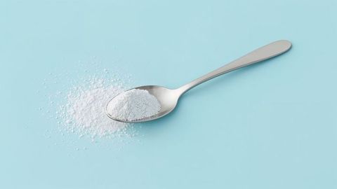 Steel spoon with white milk powder on pastel blue surface