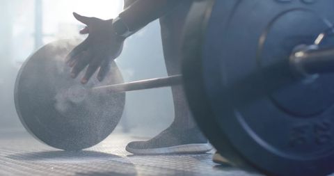Chalking hands preparing heavy deadlift with barbell plates and chalk dust in gym