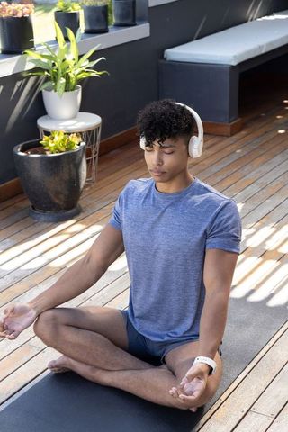 African american male meditating on balcony deck wearing headphones and fitness tracker