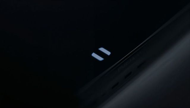 Glossy device closeup displaying illuminated pause icon in dim high-contrast studio