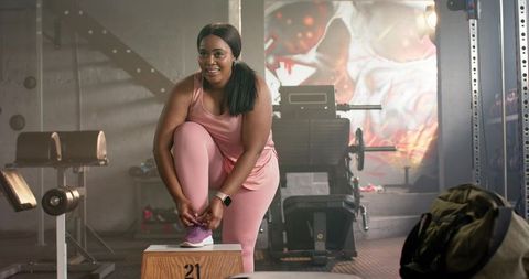 Confident african american woman tying sneakers on plyo box in industrial gym