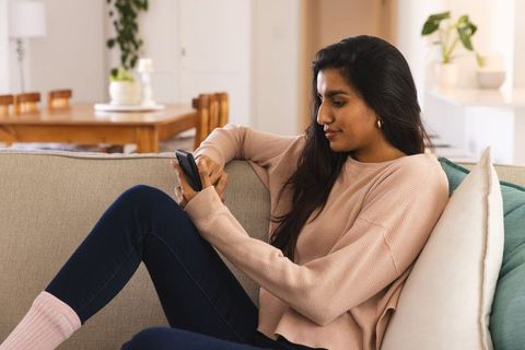 Young Woman Relaxing Using Smartphone at Home on Comfortable Couch