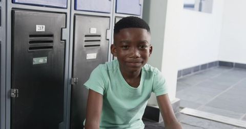 Teenage boy sitting beside school lockers smiling calmly in minimalist hallway daylight