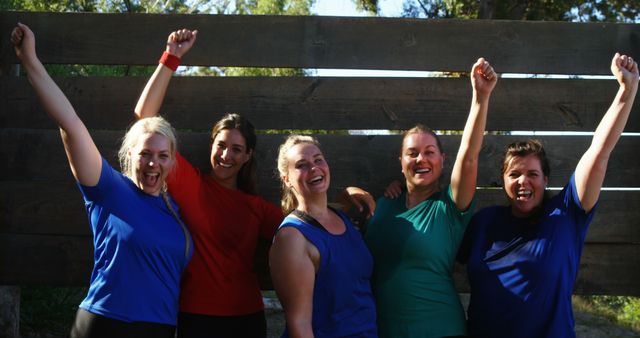 Five women standing together outdoors with raised arms and smiles, celebrating a team success. Suitable for concepts related to friendship, unity, teamwork, and outdoor activities. Useful for advertisements, motivational resources, and sports-related content.