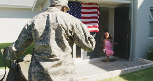 Image shows a military father in uniform joyfully reuniting with his daughter at home, an American flag displayed in the background. Suitable for use in stories related to military family reunions, patriotic events, Veterans Day, and advertising for military family-support services.